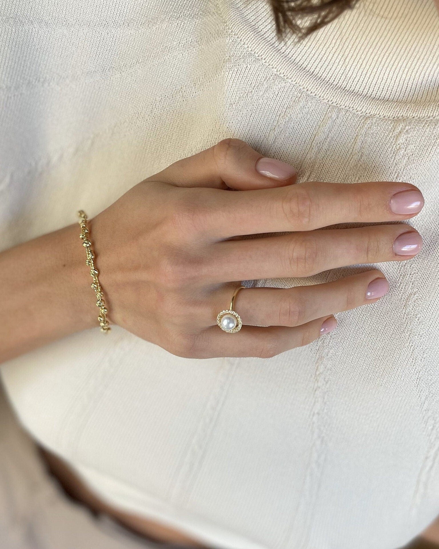 Close-up of a person wearing a gold bracelet and ring on a white shirt.