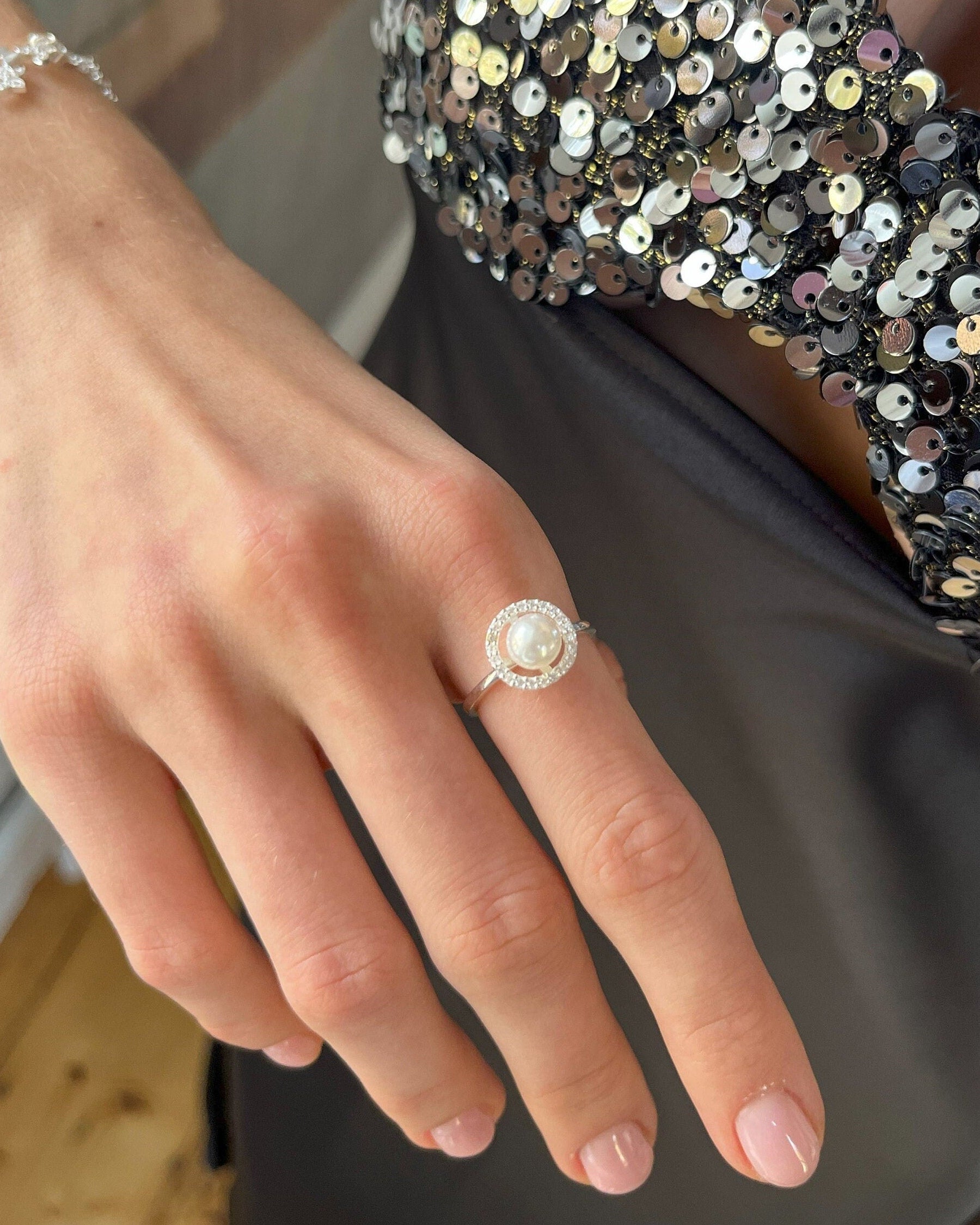 Hand wearing a pearl ring with sequined sleeve in the background