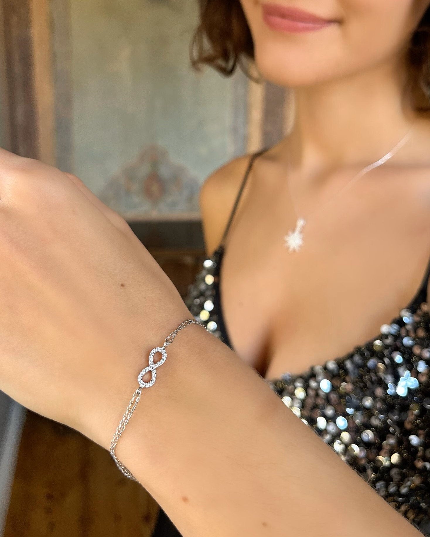 Woman wearing a silver bracelet and necklace with a sequined top.