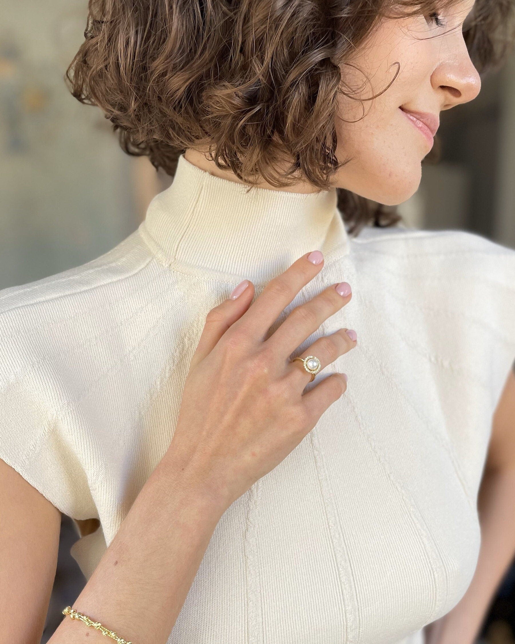 Woman wearing a white blouse with a high collar, holding her hand to her chest.
