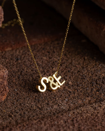 Gold necklace with 'S&E' pendant on a textured brown surface