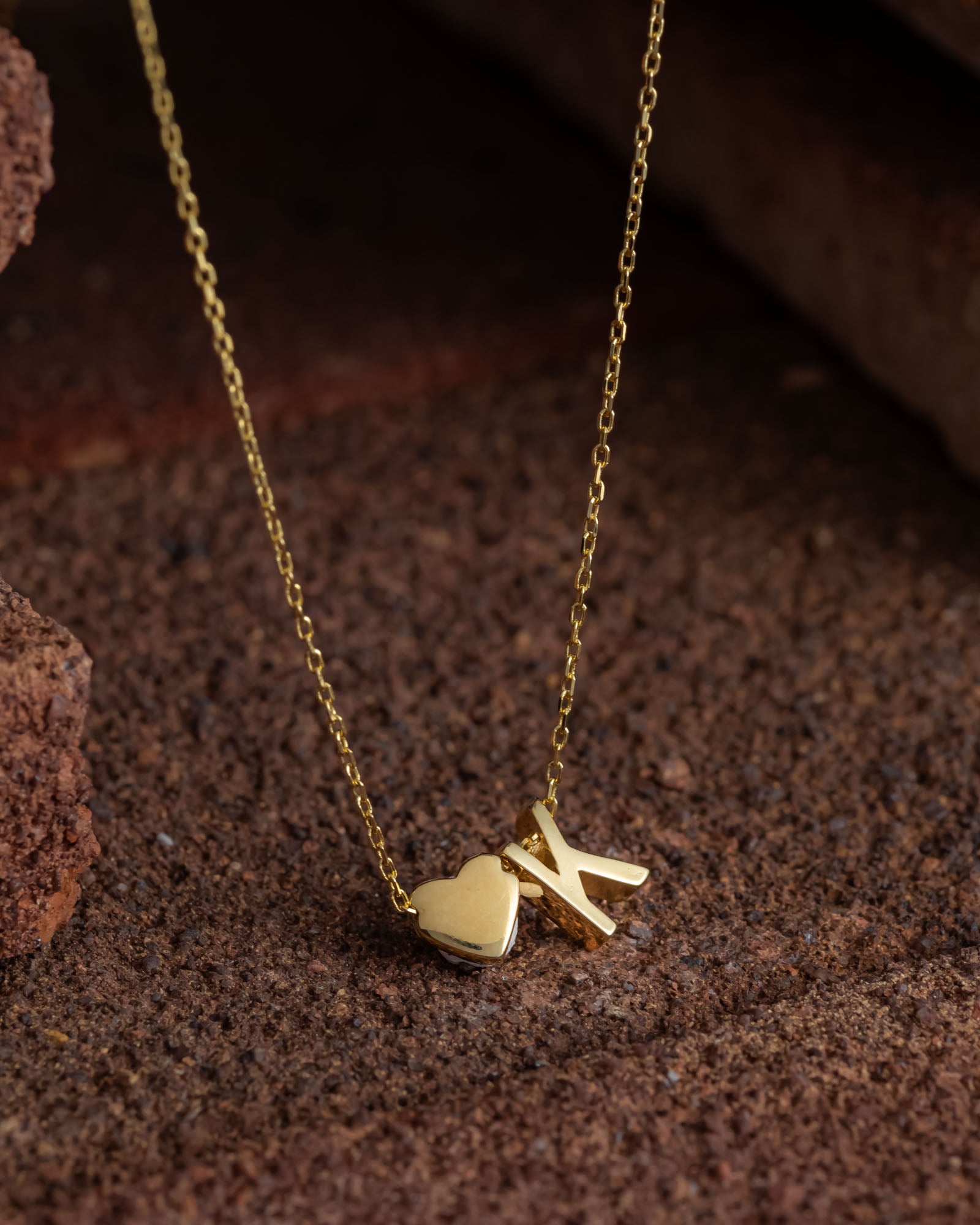 Gold necklace with a heart and 'X' pendant on a textured brown surface