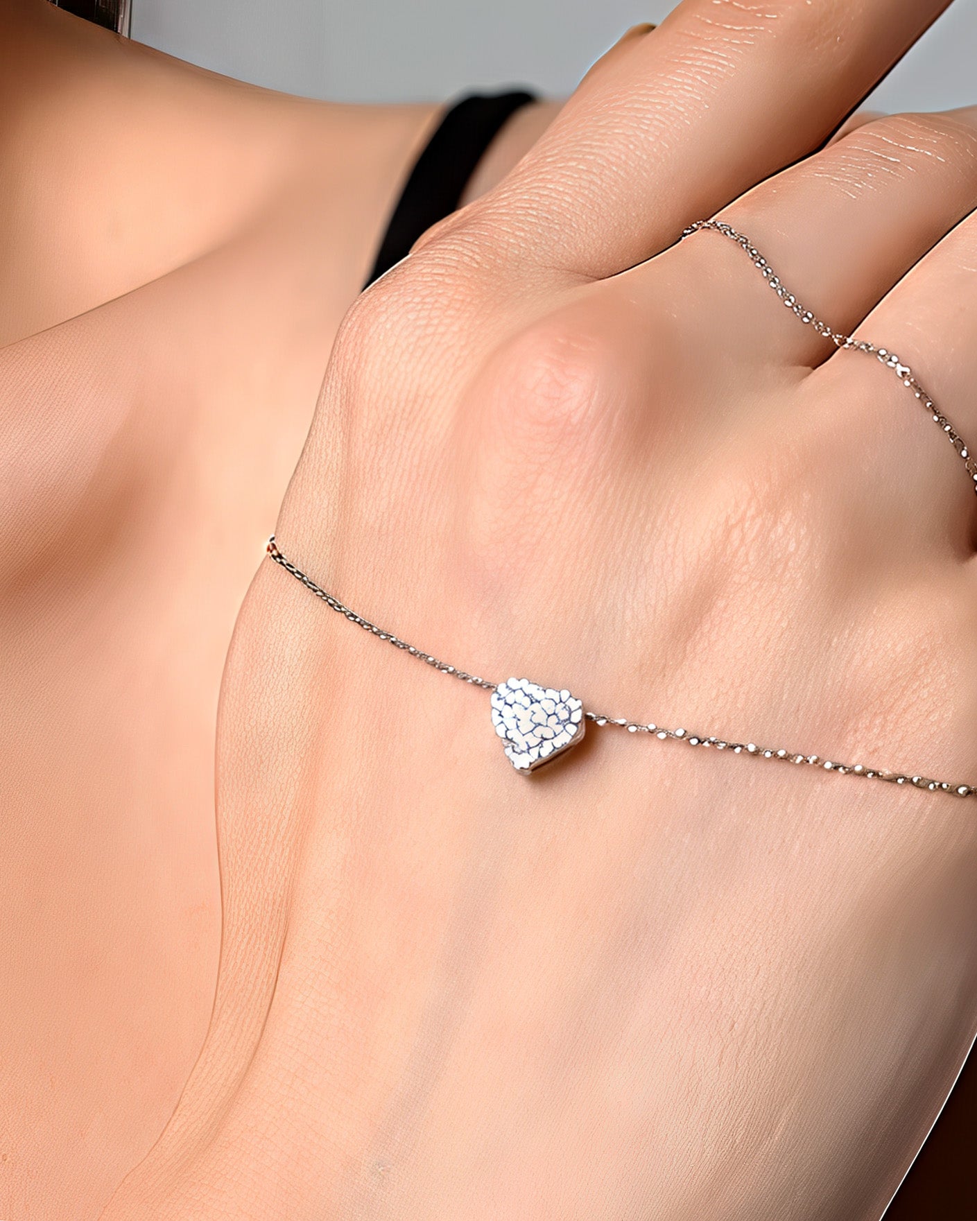 Heart-shaped diamond bracelet on a hand against a neutral background