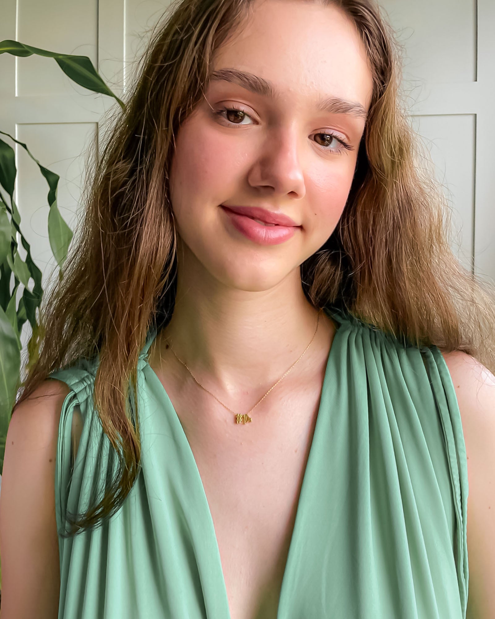Woman wearing a green dress with a white paneled wall and plant in the background