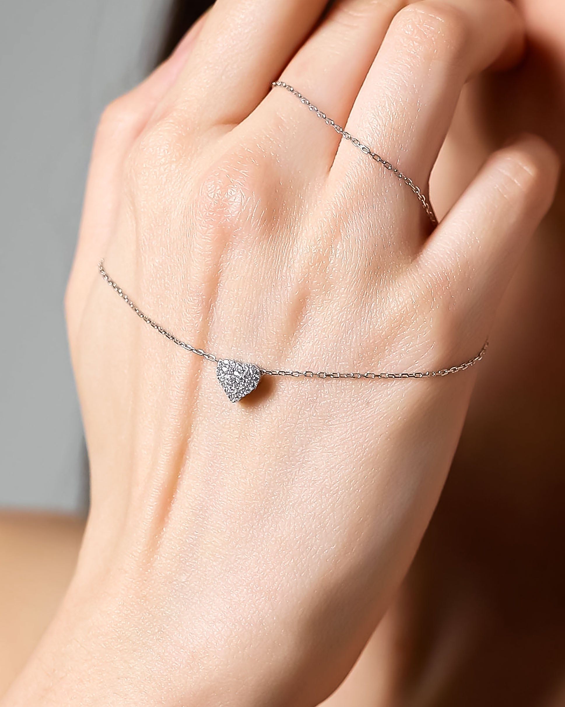 Silver heart-shaped bracelet on a hand against a neutral background