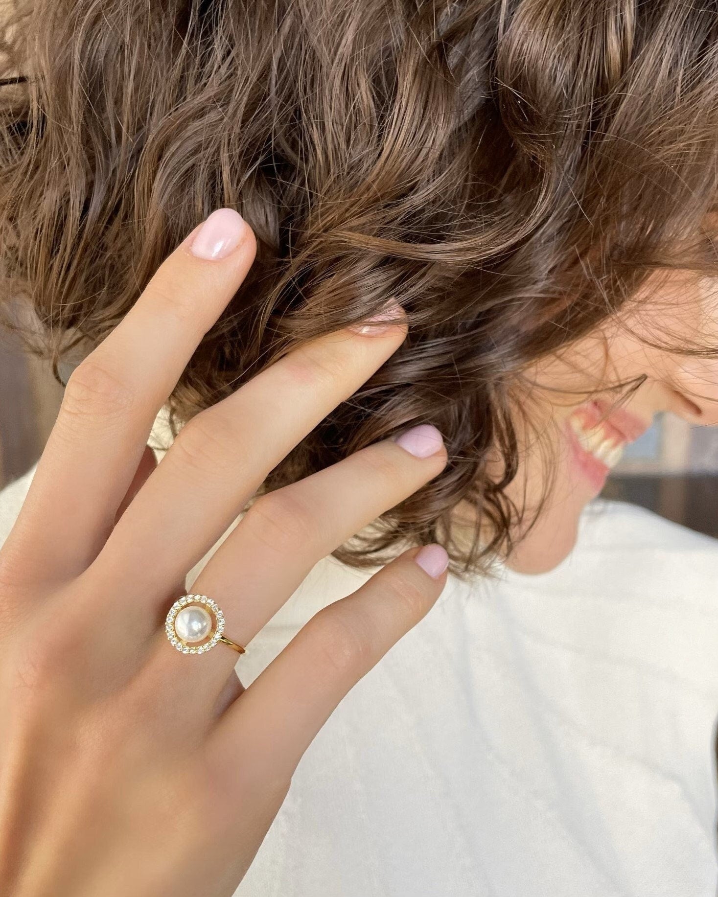 Close-up of a hand wearing a gold ring with a pearl, touching hair.