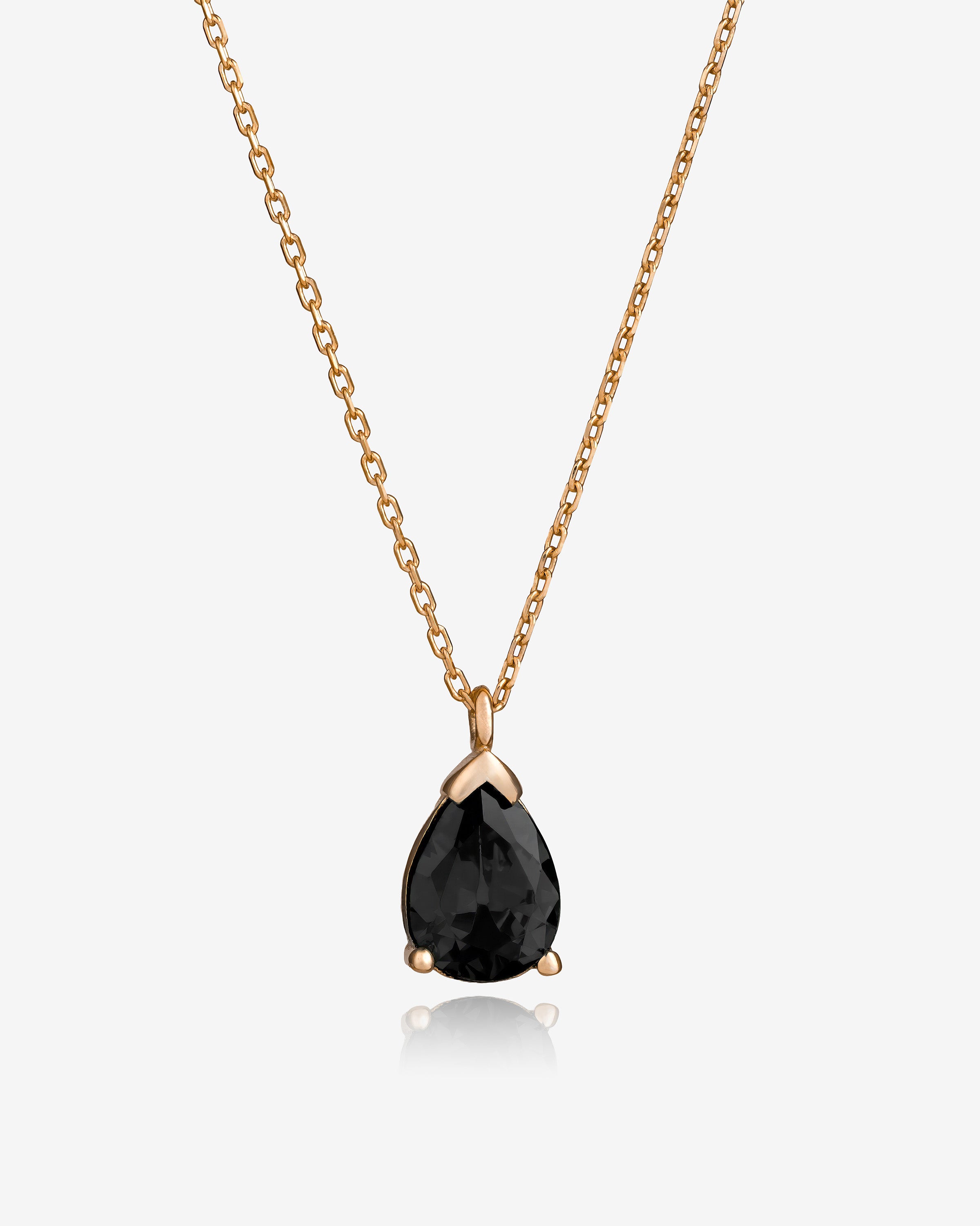 Gold necklace with a black teardrop pendant on a white background
